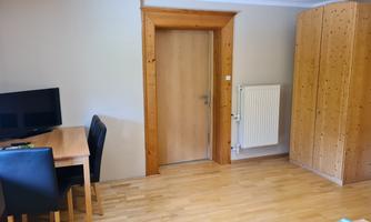 A simple room with wooden flooring. There is a table with chairs, a television, and a wardrobe.