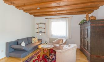 A cozy living room with a wooden ceiling and a comfortable sofa. The room is decorated with a carpet, a cozy seating area, and a traditional cupboard.