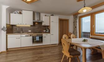 A modern kitchen with bright cabinets and a dining table. Large windows let in plenty of light and offer a view outside.