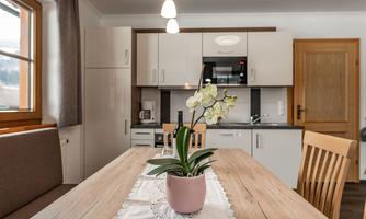A modern kitchen with an oval table and wooden chairs. In the center, there's a flower pot with an orchid.
