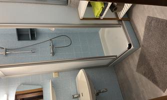 A modern bathroom with a shower cabin and a sink. The walls are tiled in light blue and there is a towel rack with fresh towels.
