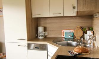 A modern kitchen with white cabinets and a dark cooktop. On the countertop, there is a loaf of bread next to kitchen utensils.