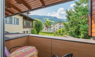 A view of a terrace with a table and chairs. In the background, green mountains and houses are visible.