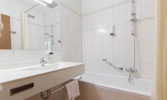A modern bathroom with a bathtub and a sink. The walls are tiled and there is a large mirror.