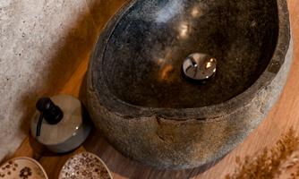 An elegant stone sink on a wooden shelf. Next to the sink are decorative bowls and a gray vessel placed.