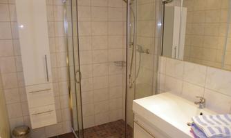 A modern bathroom with a glass shower and bright, elegant furnishings. The sink area is clean and well-organized.