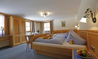 A cozy room with two beds, a table, and wooden paneling. There is fresh fruit on the table and many windows that let in natural light.