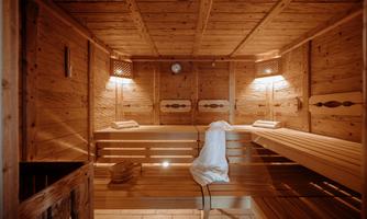 A clean wooden sauna with gentle lighting. Towels are lying on the benches, and a wooden basin is visible.