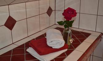 A well-maintained bathroom area with a red towel, a white towel, and a rose in a vase. The tiles are in soft, neutral colors.
