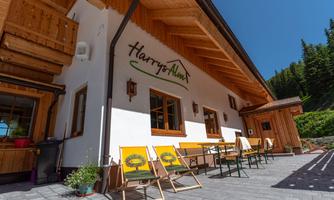 A cozy chalet in the mountains with an inviting outdoor area. Yellow chairs are ready for relaxation, surrounded by green trees.