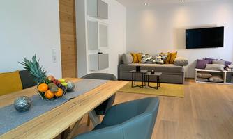 A modern living room with a gray sofa and a flat-screen TV. The table is adorned with a fruit bowl and decorative elements.