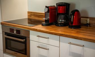 A modern kitchen with a wooden countertop. On the table, there is a coffee machine, a coffee maker, and a red kettle.