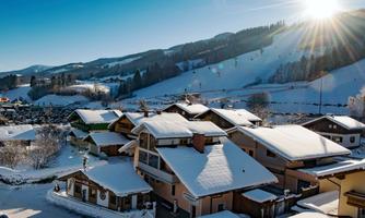 A snowy landscape with charming houses. The sun shines over the hills, creating a cozy winter atmosphere.