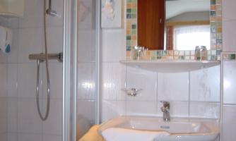 A small bathroom with a shower cabin and a sink. The mirror is mounted above the sink, and some toiletries are visible.