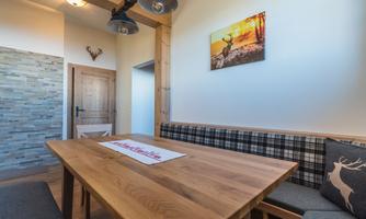 A cozy dining area with a large wooden table and a bench. The walls are light, and decorative details create an alpine atmosphere.