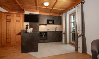 A modern kitchen with a wooden ceiling, black kitchen cabinets, and a large window. The floor is made of wood and creates a cozy atmosphere.