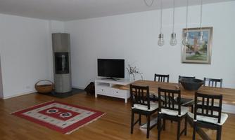 A modern living room with a dining table, chairs, and a television. The room features a carpet and a fireplace, as well as a painting on the wall.