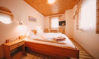 A cozy bedroom with a large bed and bright wood decor. There is a window with curtains and a television on the wall.