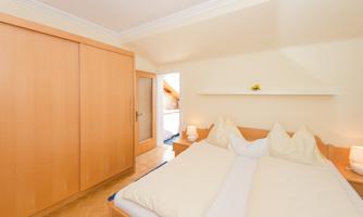 A cozy bedroom with a double bed and wooden wardrobes. The walls are adorned in soft colors and the light is bright and welcoming.