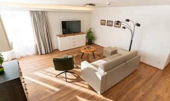 A modern living room with a cozy sofa and a round table. Large windows provide plenty of natural light and an inviting atmosphere.