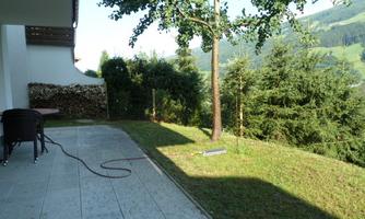A quiet garden with a well-maintained lawn and a tree. In the background, wooded hills are visible.