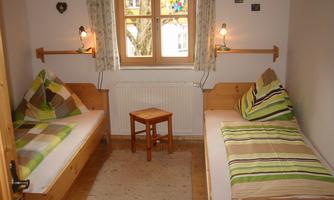 A cozy room with two beds and colorful pillows. There is a small table and a window with curtains.
