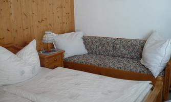 A cozy bedroom with a double bed and a small sofa. The walls are paneled with wood, and there are cushions on the bed and the sofa.