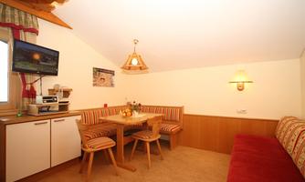 A cozy living area with wooden paneling and a table. The seating area is decorated with red and white fabrics, and there is a television on the wall.