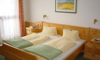 A cozy bedroom with a wooden double bed. The walls are light, and a picture hangs above the bed.