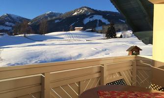 A balcony with a view of a snowy landscape and snow-covered mountains. The sun is shining and the sky is clear.