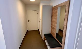 A modern hallway with a black seating area and a large mirror. The walls are bright and the floor is made of dark wood.