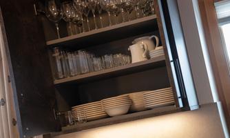 A shelf with glassware and dishes. Glasses are on top and plates as well as a jug are at the bottom.