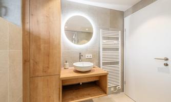 A modern bathroom with wood and tile elements. The round mirror with lighting complements the elegant design.