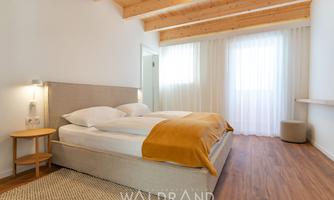 A modern bedroom with a large bed and a warm, yellow coverlet. The large windows provide plenty of daylight and a cozy atmosphere.