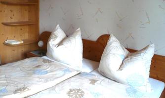 A cozy bedroom with two beds and large pillows. On the wall is a light wallpaper with colorful patterns.