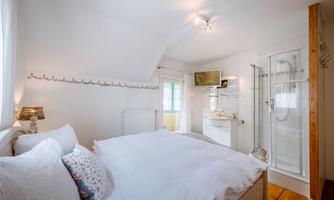 A cozy bedroom with a large bed and bright colors. In the background, there is a bathroom with a shower cubicle.