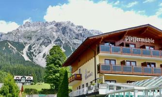 A charming hotel in the foreground named "Pfeffermühle" with an impressive mountain backdrop in the background. The surroundings are green and inviting, perfect for nature lovers.