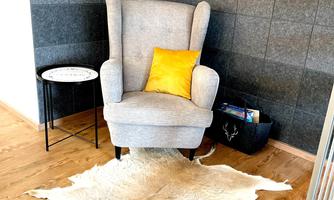 A cozy armchair with a yellow cushion is placed on a cowhide rug. Next to the armchair, there is a round table and a black box.