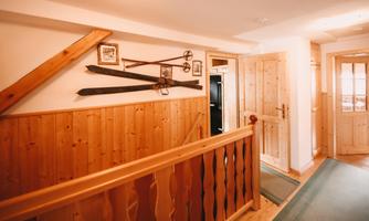An inviting hallway with wooden paneling and nostalgic skis on the wall. The doors and the carpet give the room a warm atmosphere.