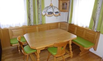 A cozy dining area with a wooden table and chairs. The walls are light, and the windows have green curtains.