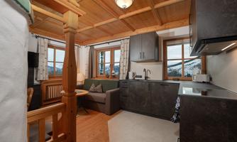 A cozy vacation apartment with wooden furniture, a sofa, and a modern kitchen. Large windows offer a view of the mountains.