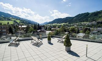 A spacious balcony with loungers and a view of a picturesque mountain landscape. The surrounding mountains and clear weather create an inviting atmosphere.