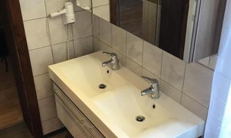 A modern bathroom with a double washbasin and two sinks. A large mirror reflects the room, which is decorated with tiles and a red carpet.