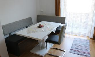 A modern dining area with a white table and an elegant seating arrangement. The room is bright and welcoming with curtains and a colorful carpet.