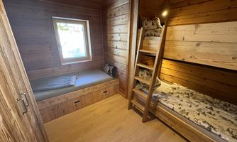 A cozy wooden room with a window and two beds. The walls are also made of wood, creating a warm atmosphere.