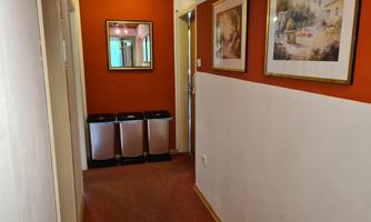 A corridor with orange walls and several pictures. At the end of the corridor, there are three trash bins.