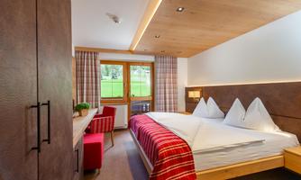 A modern bedroom with two beds and a cozy red blanket. Large windows offer a view of the green landscape outside.