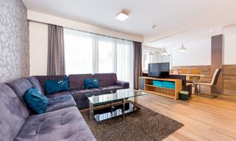 A modern living room with a comfortable purple sofa and a glass table. Large windows let in plenty of natural light.