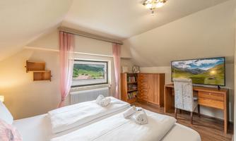 A cozy bedroom with two beds and a desk. The room has large windows and a television that shows a nice view.
