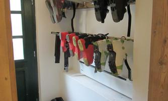 An entrance area with a shelf that holds several climbing harnesses and shoes. Next to the shelf is a sports bag.